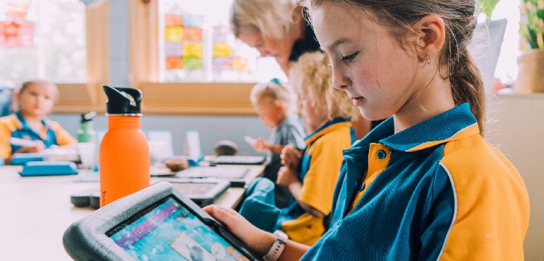 A young girl sits at her desk looking at an Ipad. 